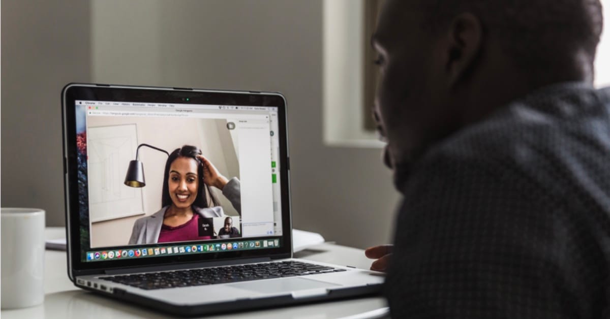A shot of a video conference with a woman who can be seen smiling on screen. A man is sitting in front of the computer.