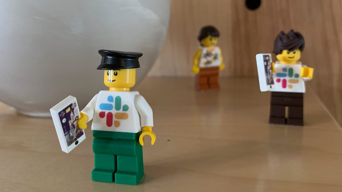 Three lego minifigs. They are wearing Slack logo tops, and holding mobile phones.